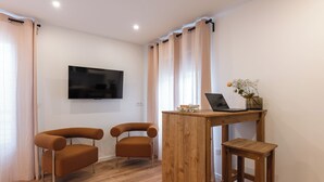 A modern living room with a flat-screen TV mounted on the wall, two brown armchairs, a wooden coffee table with a laptop and decorative items, and light-colored curtains. - LA VILLA Le Bourget Paris Parc des Expos (Le Bourget)