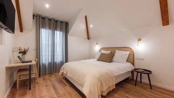 Une chambre à coucher comprenant un lit, un bureau, une chaise, une petite table et une fenêtre avec des rideaux.