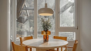 Una mesa redonda de comedor con seis sillas de madera, un jarrón con flores y una lámpara colgante.