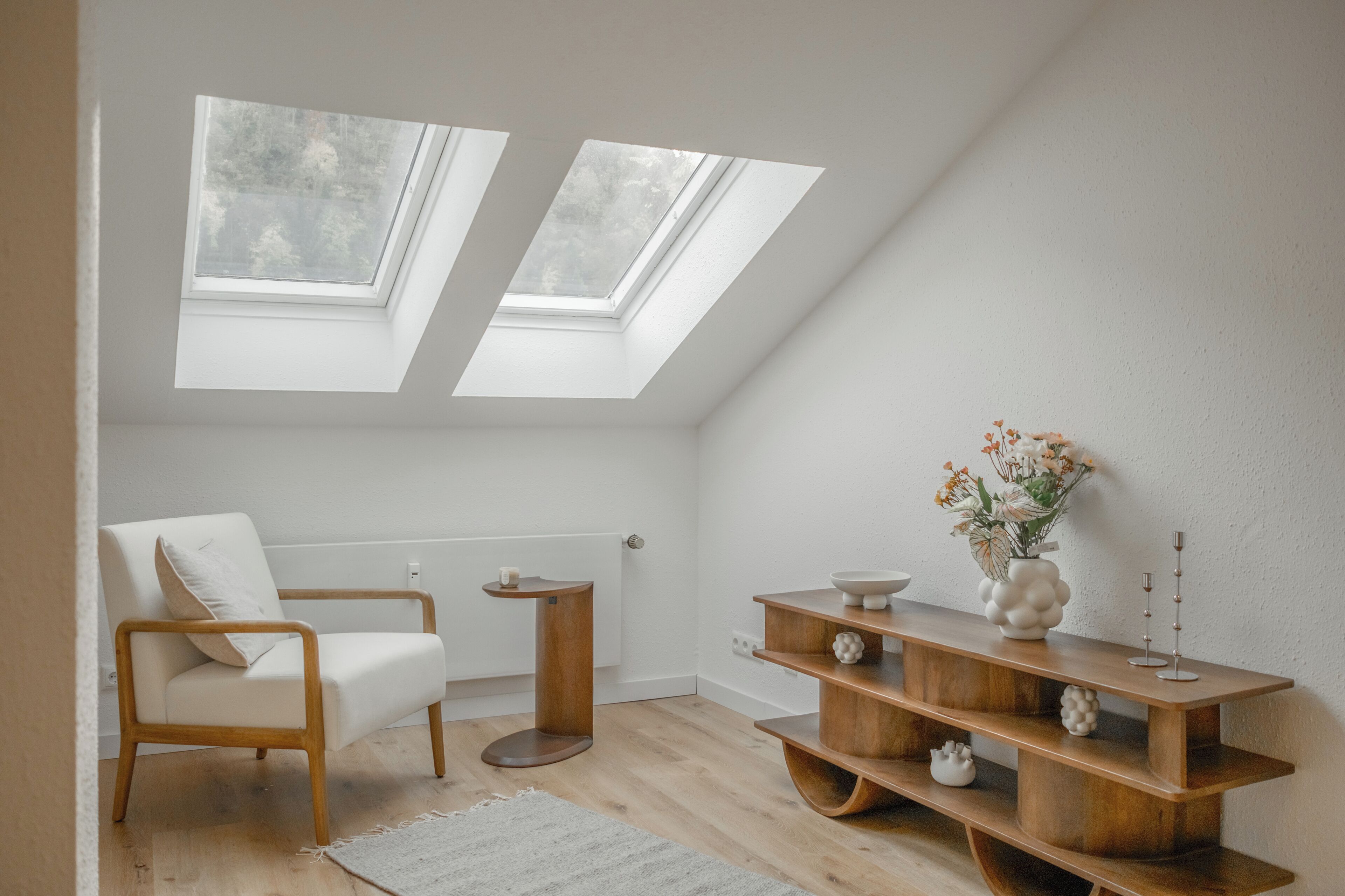 Une chambre de style loft moderne, dotée de fenêtres de toit, d’une chaise en bois, d’une petite table d’appoint et d’une console en bois agrémentée d’objets décoratifs.