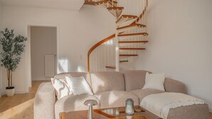 Una sala de estar moderna con una escalera curva, un amplio sofá modular y una mesa de centro de vidrio.