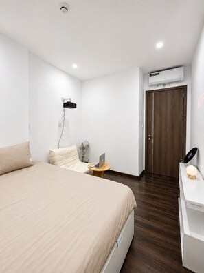 A modern hotel room with a bed, a desk with a laptop, a fan, and a door. - X-Stay Sweet (Hai Phong)