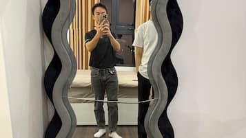 A mirror with a wavy frame in a room with a wooden floor and a door in the background.