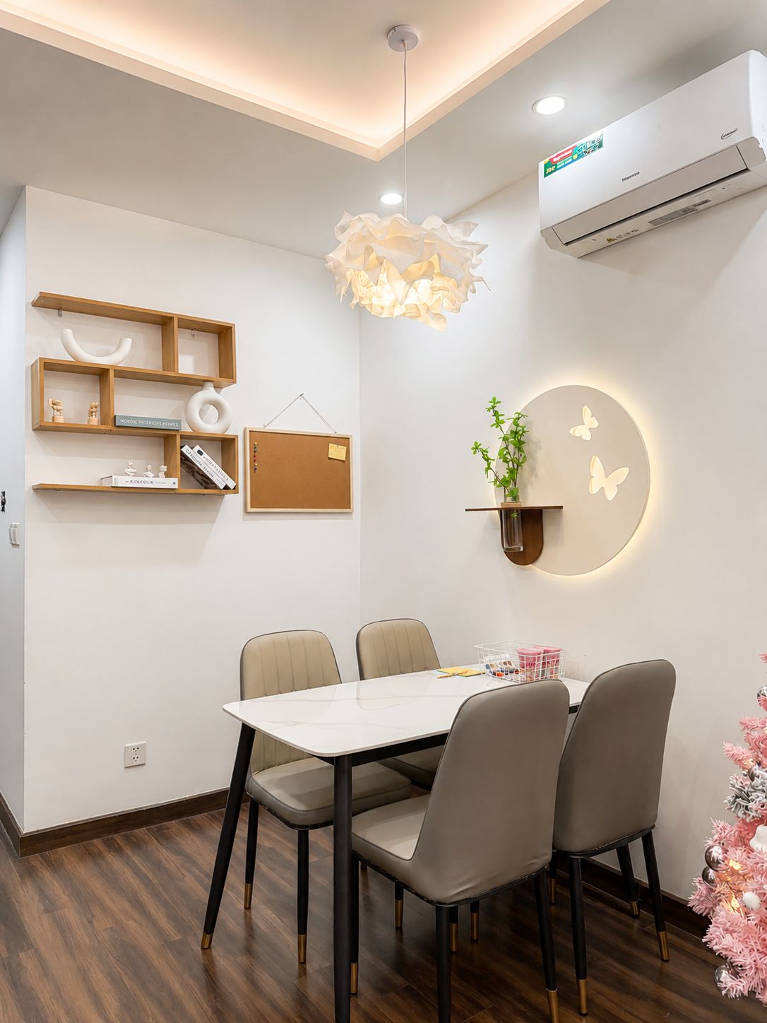 A modern dining area with a table, chairs, a hanging light fixture, a wall-mounted air conditioner, and a decorative plant.
