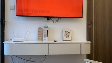 A modern room with a mounted TV displaying a motivational quote, a white console table with a router and a framed picture, and a white coffee table with a book titled "HOMES".