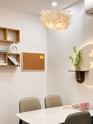 A modern dining area with a white table, two chairs, a corkboard with notes, and a hanging light fixture. - X-Stay Sweet (Hai Phong)