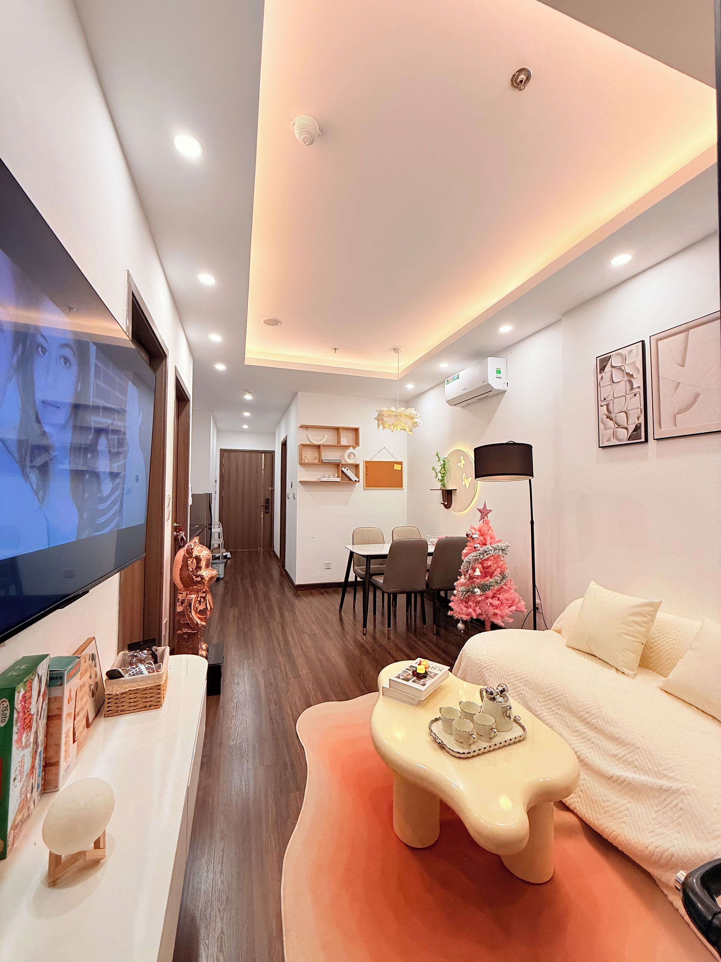 A modern living room with a flat-screen TV, a small Christmas tree, a sofa, and a dining area with chairs and a table.