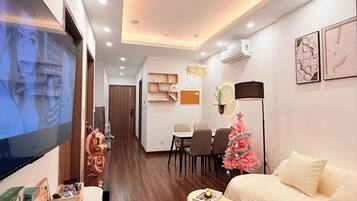 A modern living room with a flat-screen TV, a small Christmas tree, a sofa, and a dining area with chairs and a table.