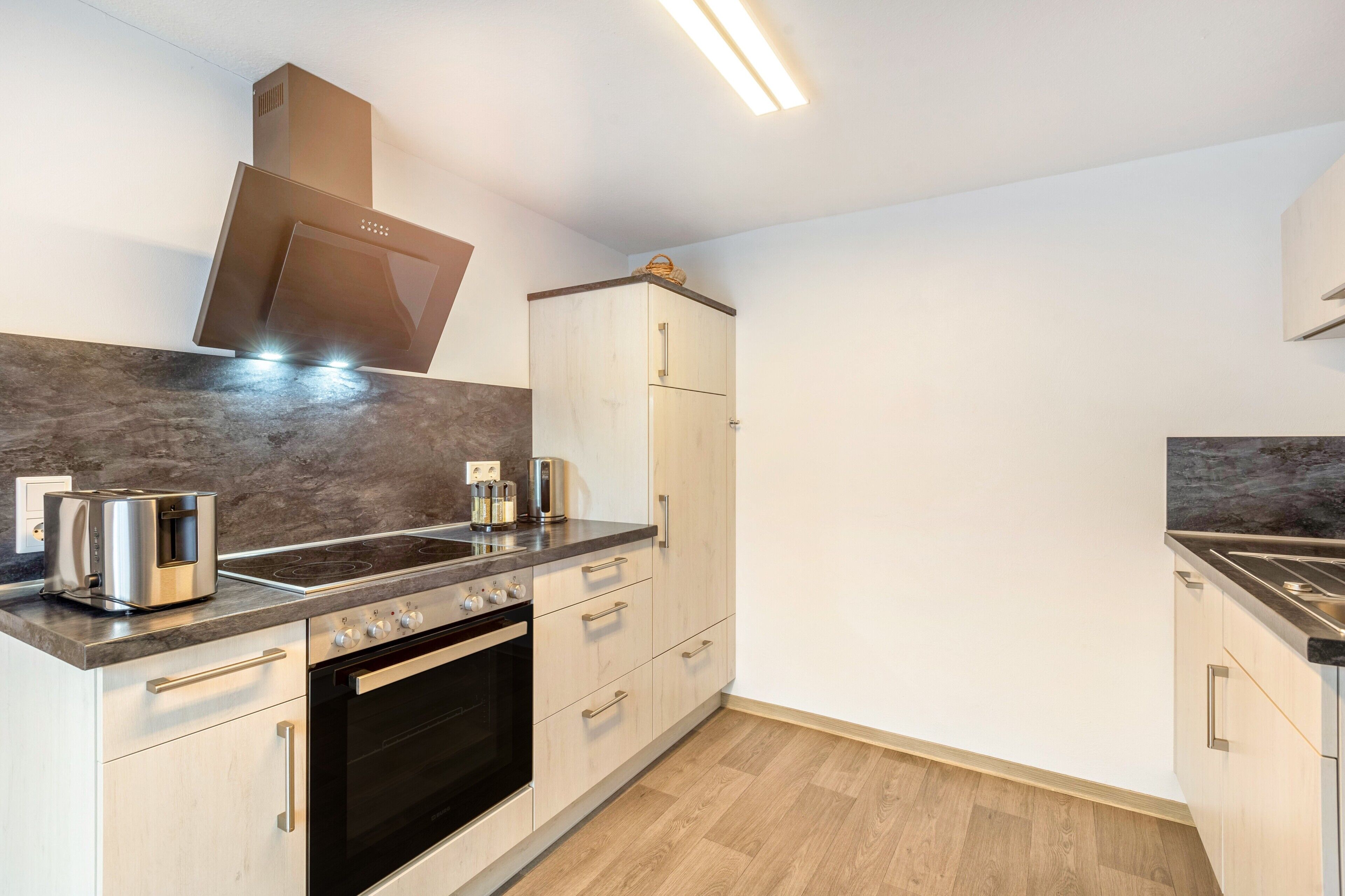 A modern kitchen with a built-in oven, a stovetop, a range hood, and a refrigerator.