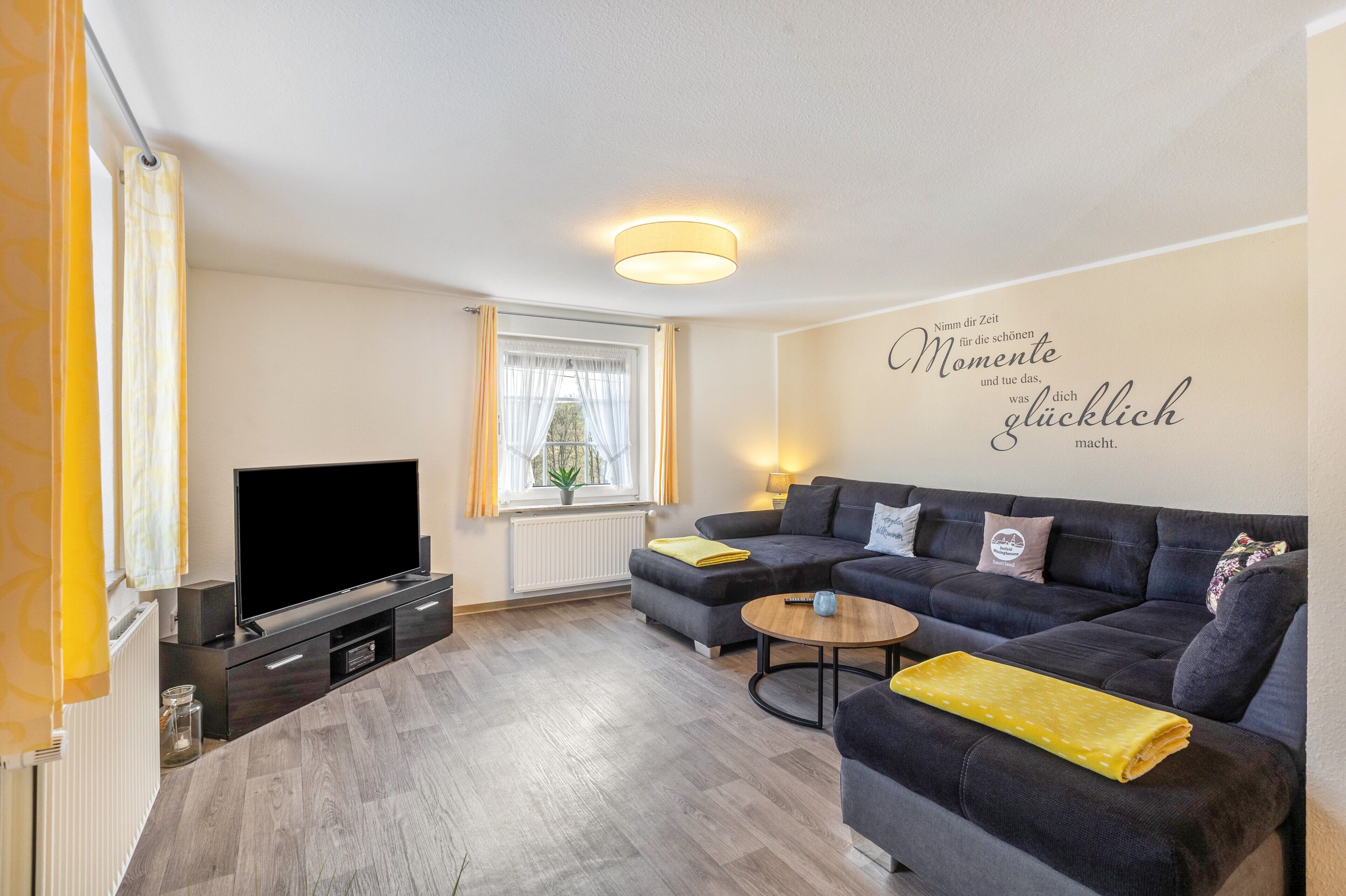 A modern living room with a flat-screen TV, a sofa, a coffee table, and a wall with a motivational quote.