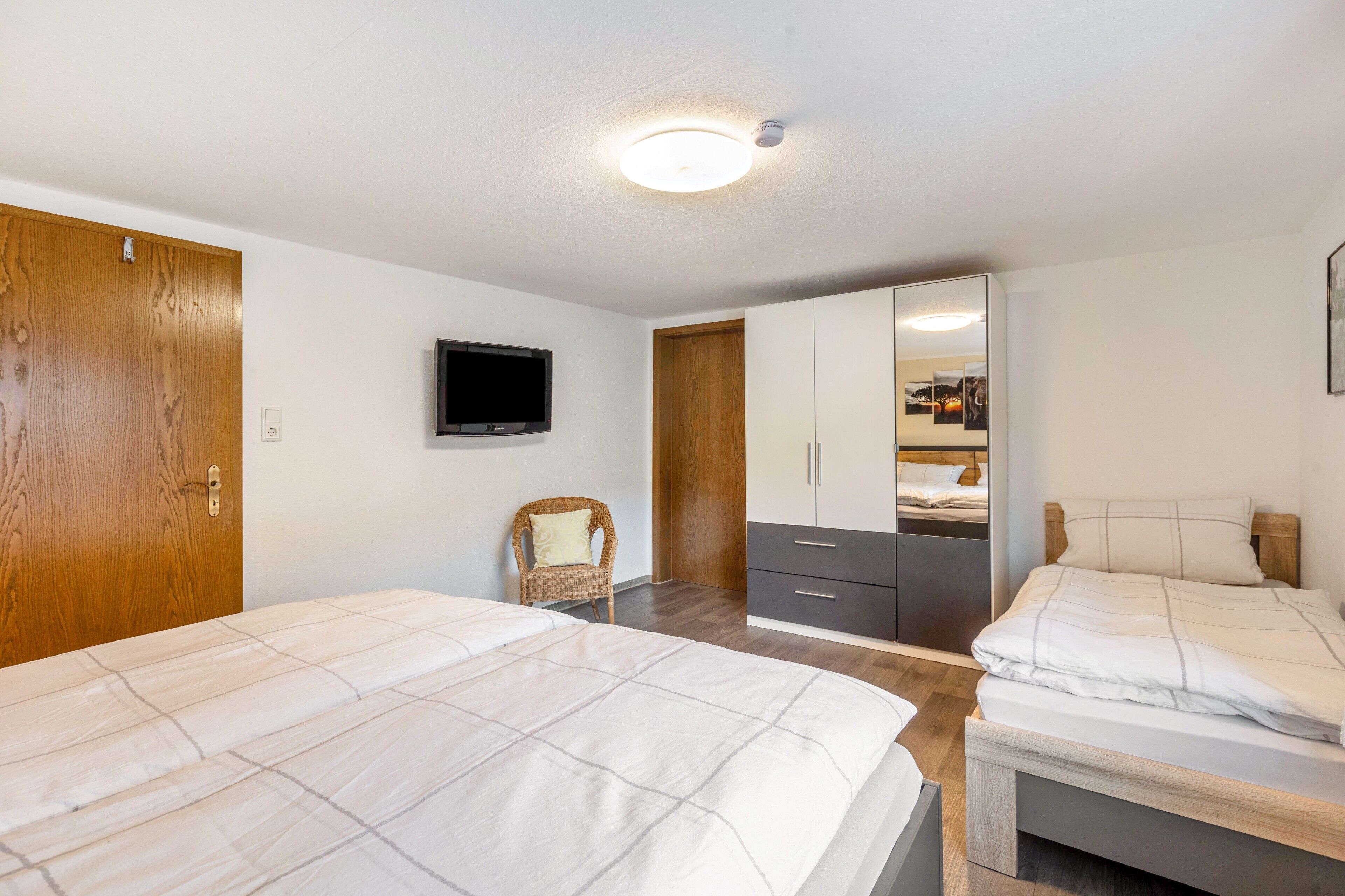 A bedroom with two beds, a television, a wardrobe, and a mirror.
