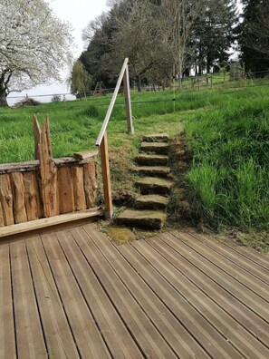 A wooden deck with stone steps leading to a grassy area.