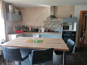 A modern kitchen with a wooden table, two chairs, a gas stove, a microwave, and a toaster.