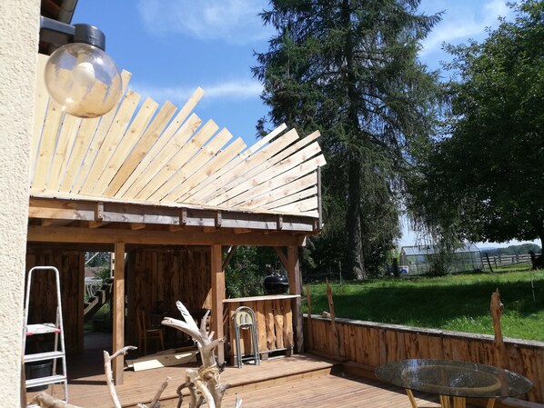A wooden deck with a pergola, a metal table, and a ladder.