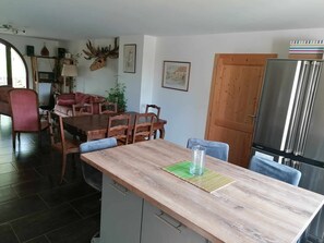 A dining area with a wooden table, chairs, and a kitchen area with a refrigerator.