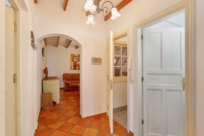 Un couloir avec un sol carrelé, une porte blanche et une pièce contenant un canapé et une lampe.
