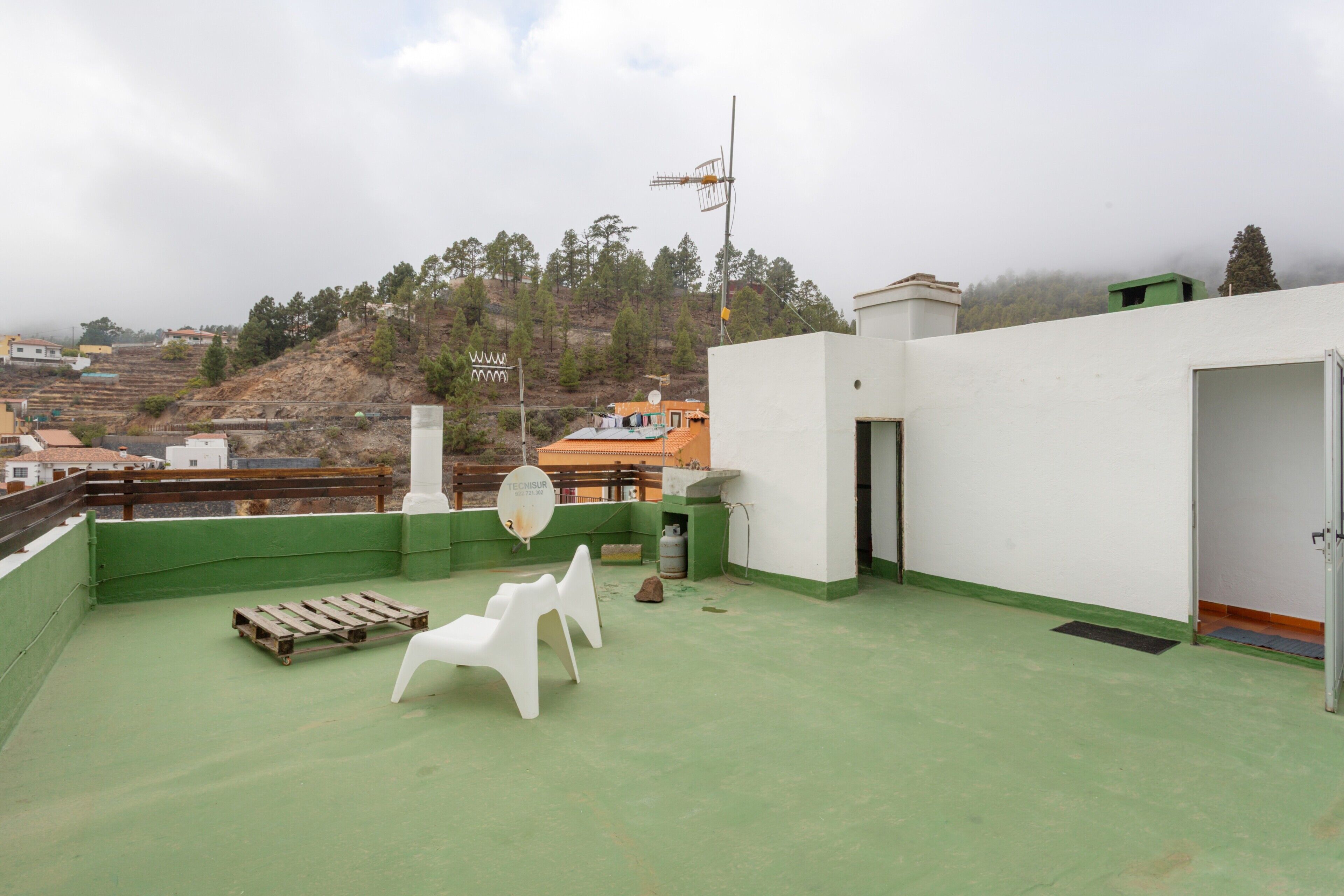 Une terrasse sur le toit, avec une antenne parabolique, un banc en bois et des chaises en plastique blanc.