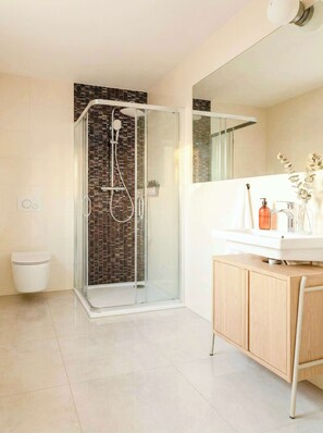 A modern bathroom with a glass-enclosed shower, a white sink with a mirror, and a wooden cabinet. - TurnKey | Antonin Dvorak Studio XIV (Praha 2)