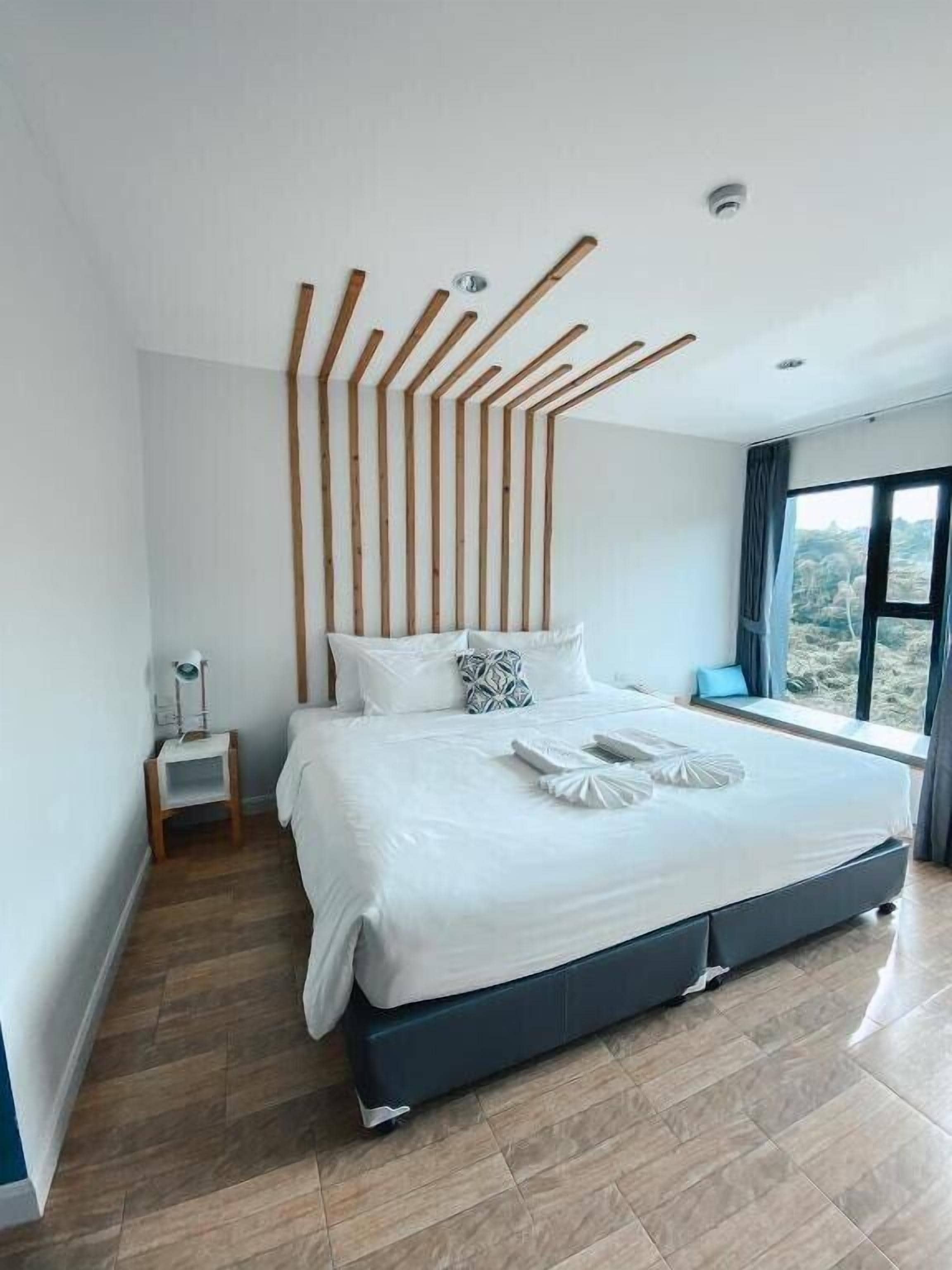 Ein modernes Schlafzimmer mit einem großen Bett, einem Nachttisch und Blick ins Freie durch ein Fenster.