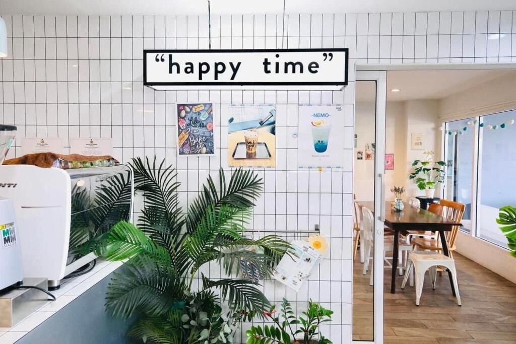 Een café interieur met een bordje met de tekst 'happy time', een toonbank met een koffiemachine en een eethoek met stoelen en een tafel.