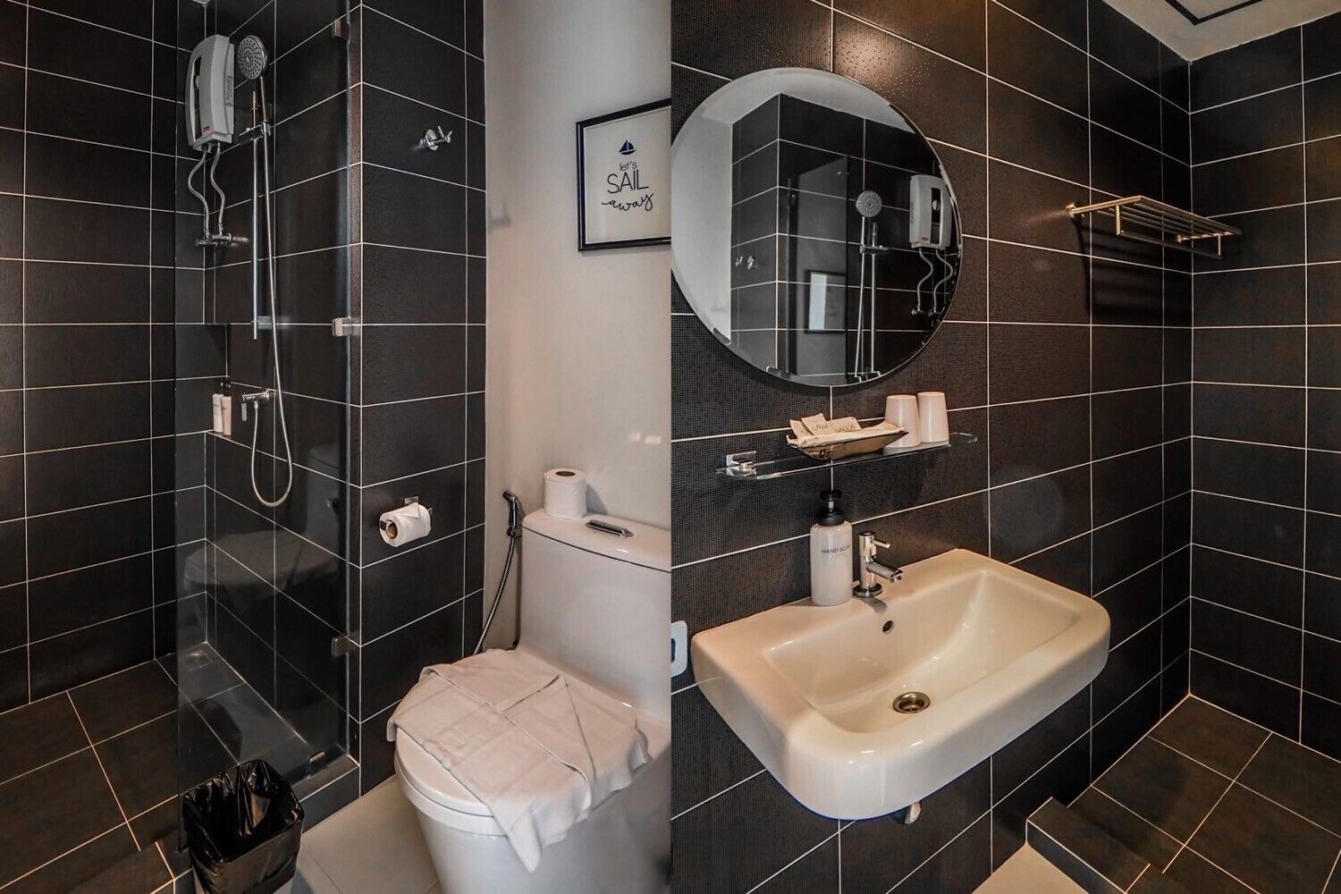 A modern bathroom with dark tiles, a white sink, a handheld showerhead, a toilet, and a framed mirror.