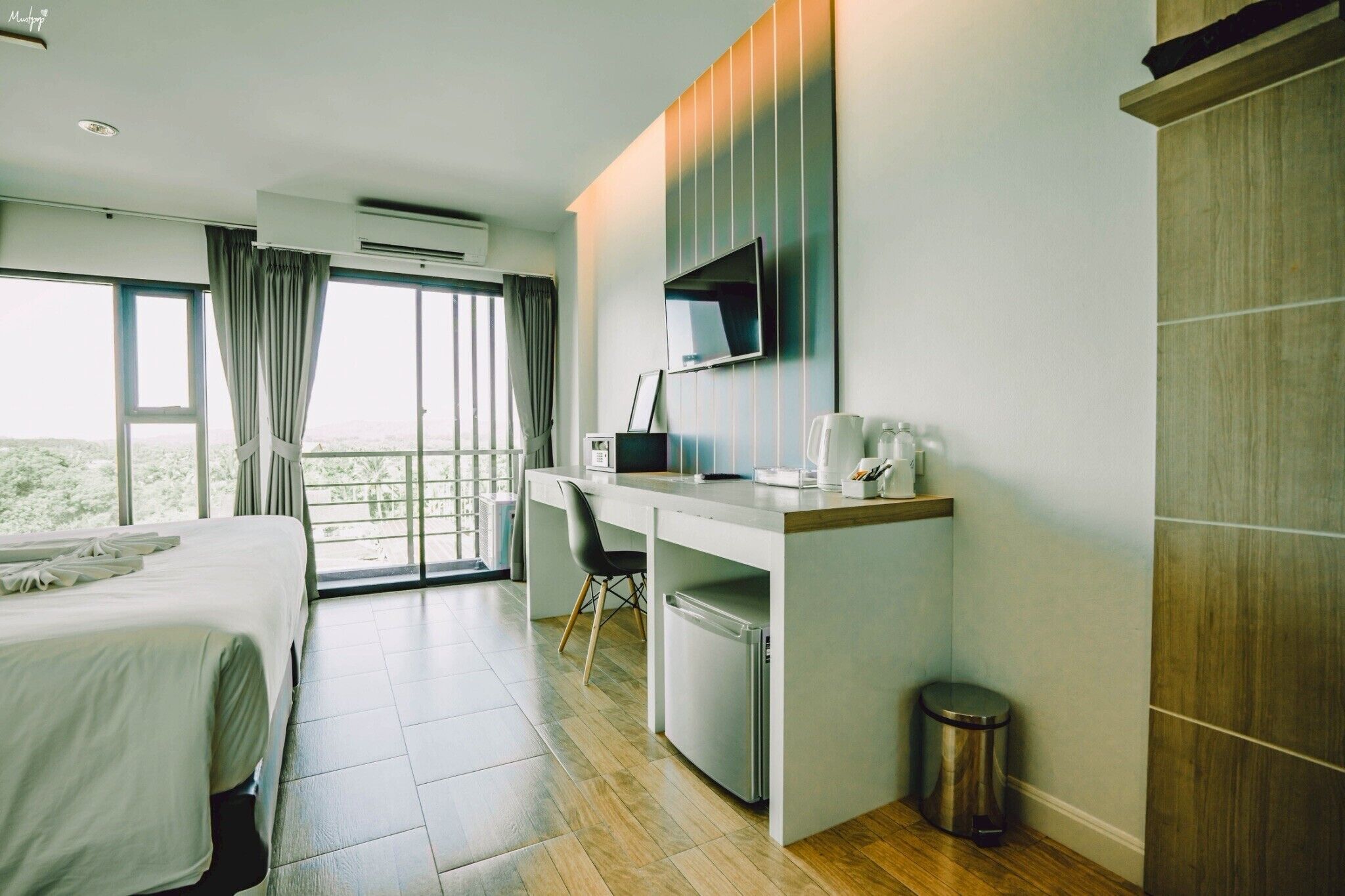 Habitación de hotel con cama, escritorio con computadora, televisor y vista al exterior.