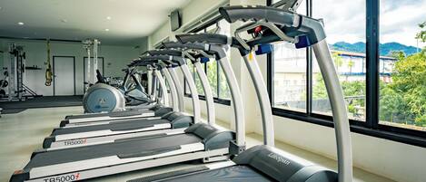 A row of treadmills in a gym with large windows and a view of buildings and mountains.