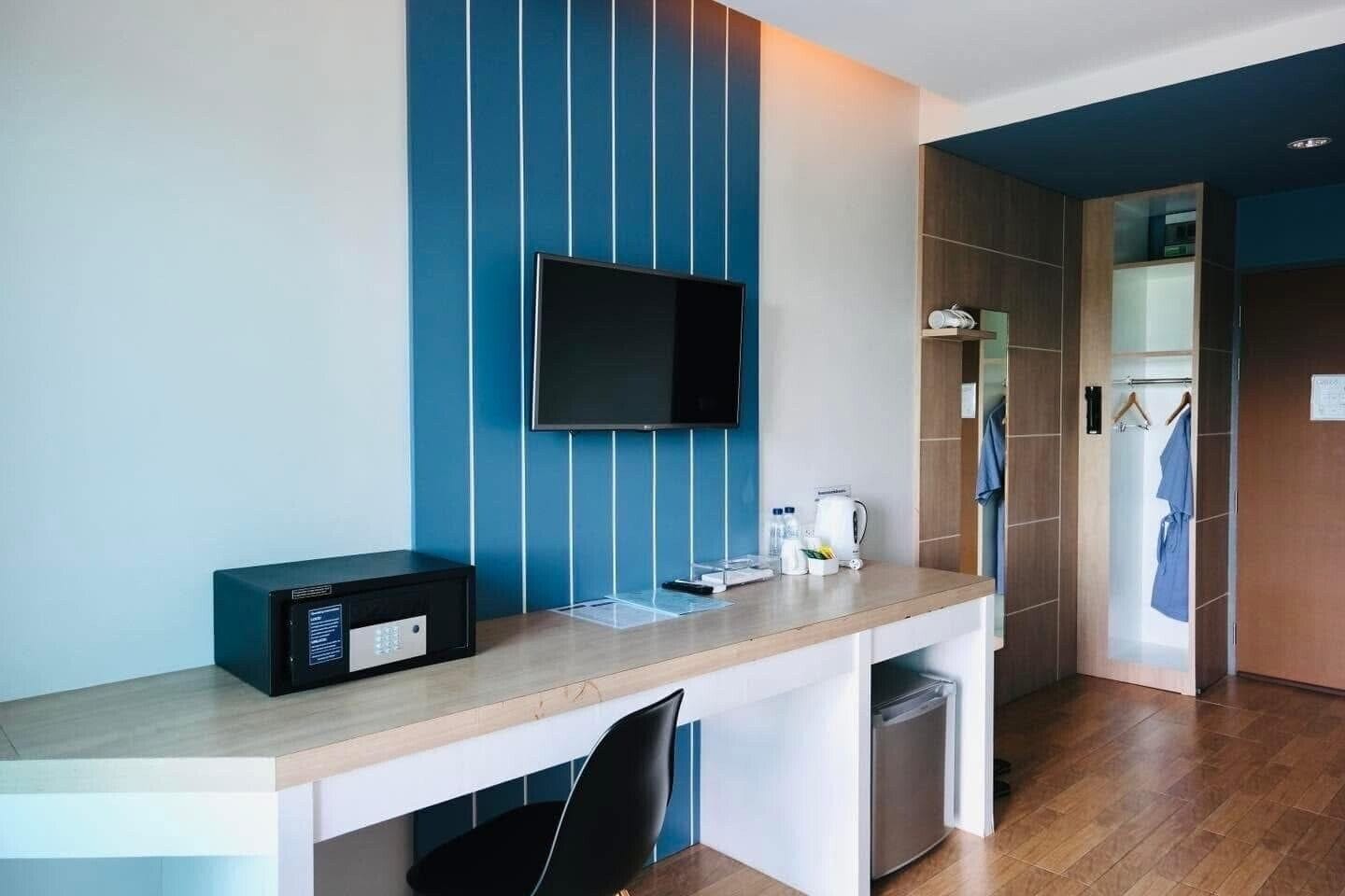 Quarto de hotel moderno com televisão de tela plana na parede, escrivaninha com micro-ondas, chaleira e pequena geladeira.