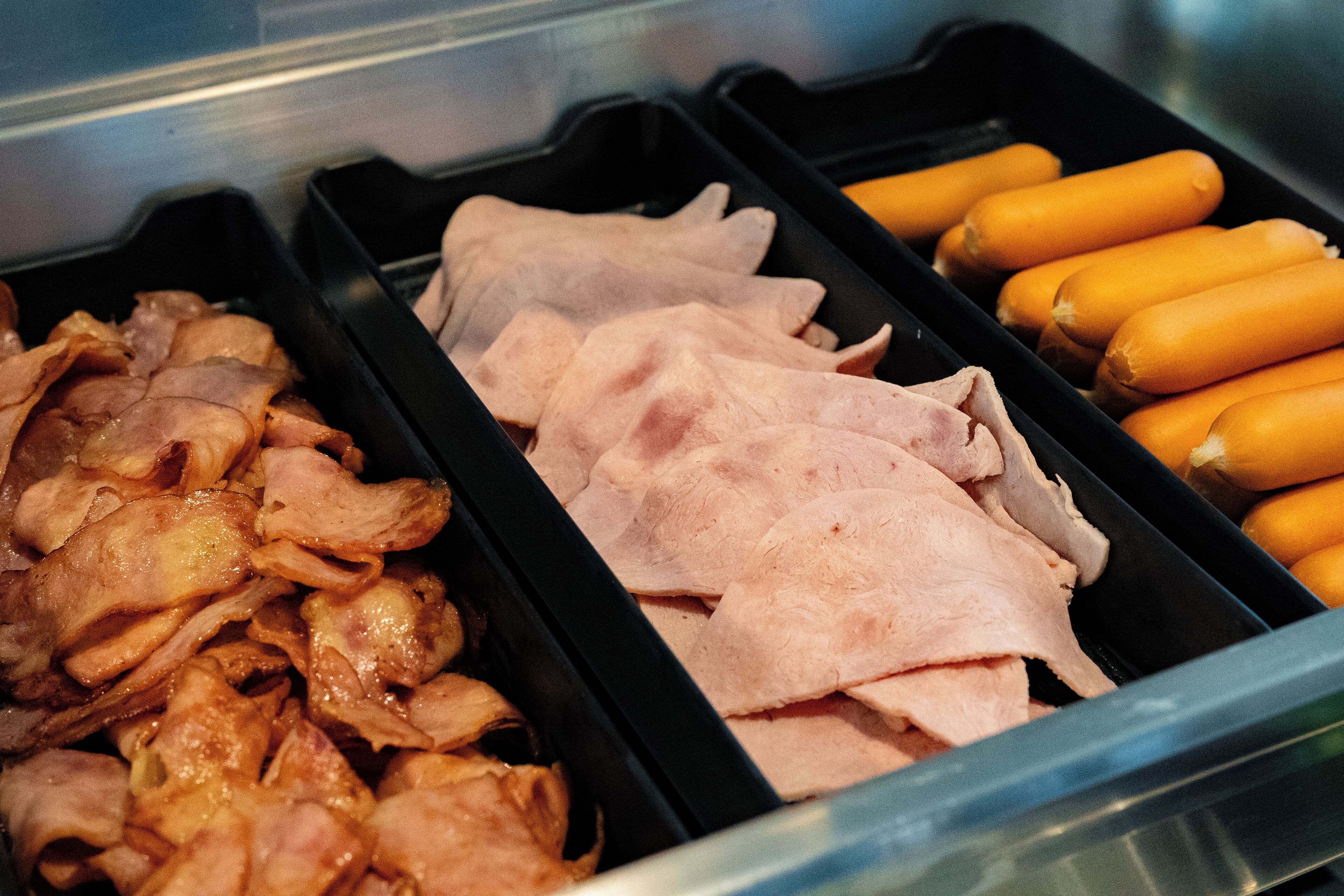 Una exposición de carnes en rodajas y salchichas en una vitrina refrigerada.