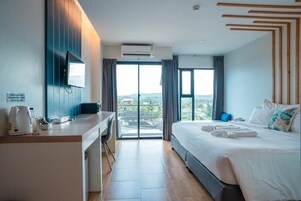 Un moderno cuarto de hotel con una cama grande, un escritorio con silla, un televisor de pantalla plana y vistas a la ciudad a través de las ventanas.