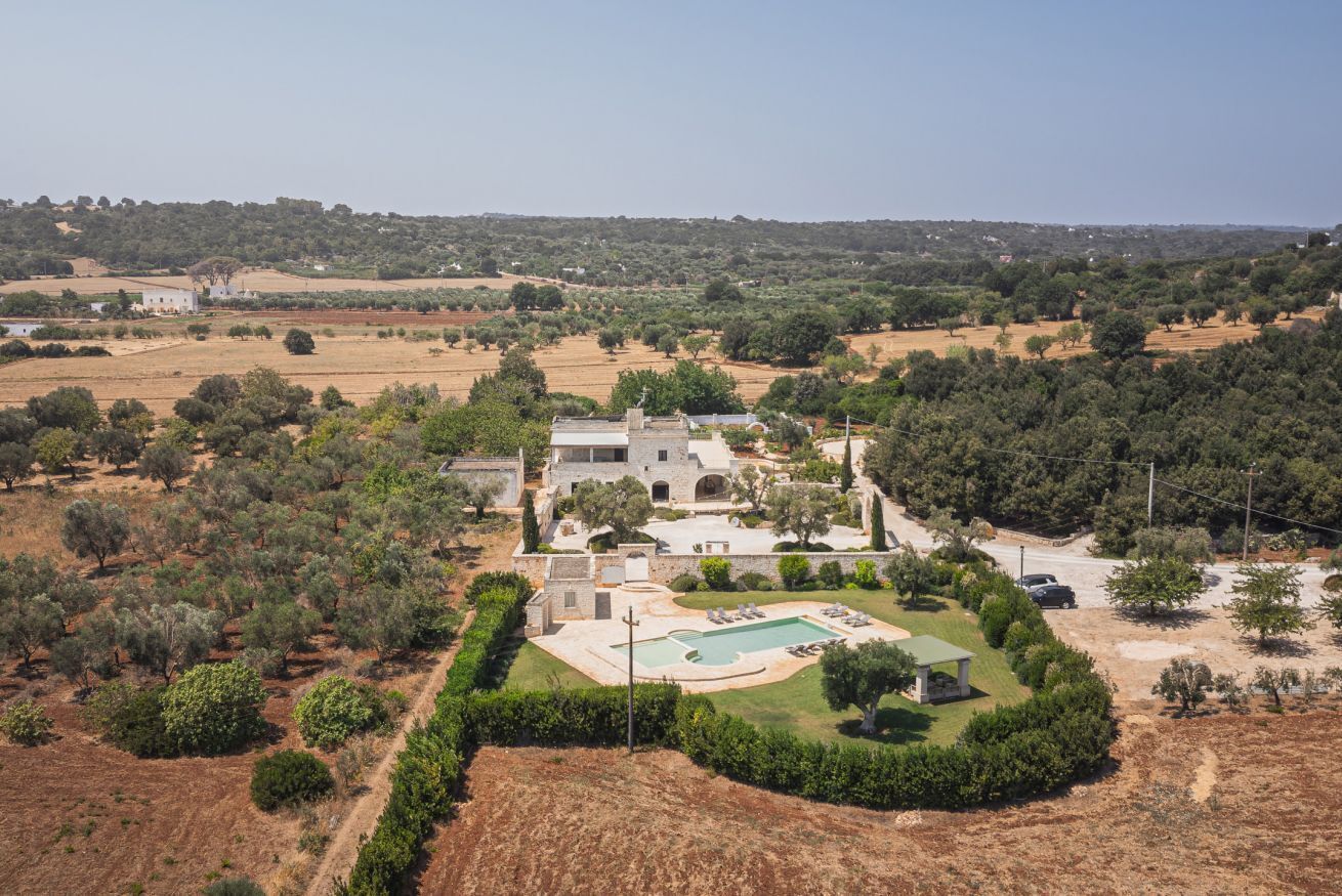 A large villa with a swimming pool, surrounded by olive groves and a hilly landscape.