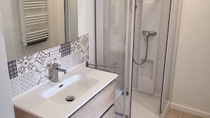 A bathroom with a white sink, wooden vanity, a glass shower enclosure, and a patterned backsplash. - Bright apartment with terrace in the heart of Morlaix (Morlaix)