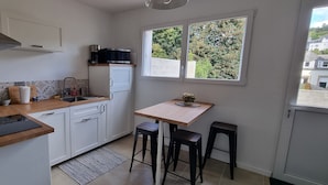 A compact kitchen with white cabinets, a wooden countertop, a sink, a coffee maker, and a window with a view of greenery. - Bright apartment with terrace in the heart of Morlaix (Morlaix)