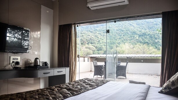 A hotel room with a bed, a desk with a television, a coffee maker, and a view of a balcony with chairs. - HOTEL HELLO JEYPORE (Jaypur)
