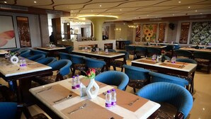 A restaurant with multiple tables and blue cushioned chairs, each set with cutlery and bottled water. - HOTEL HELLO JEYPORE (Jaypur)