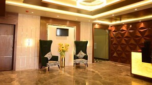 A lobby with two green armchairs, a vase with sunflowers, a TV on the wall, and a geometric patterned wall. - HOTEL HELLO JEYPORE (Jaypur)