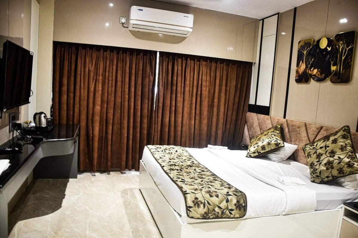 A hotel room with a bed, a desk, a flat-screen TV, and a large window with curtains.