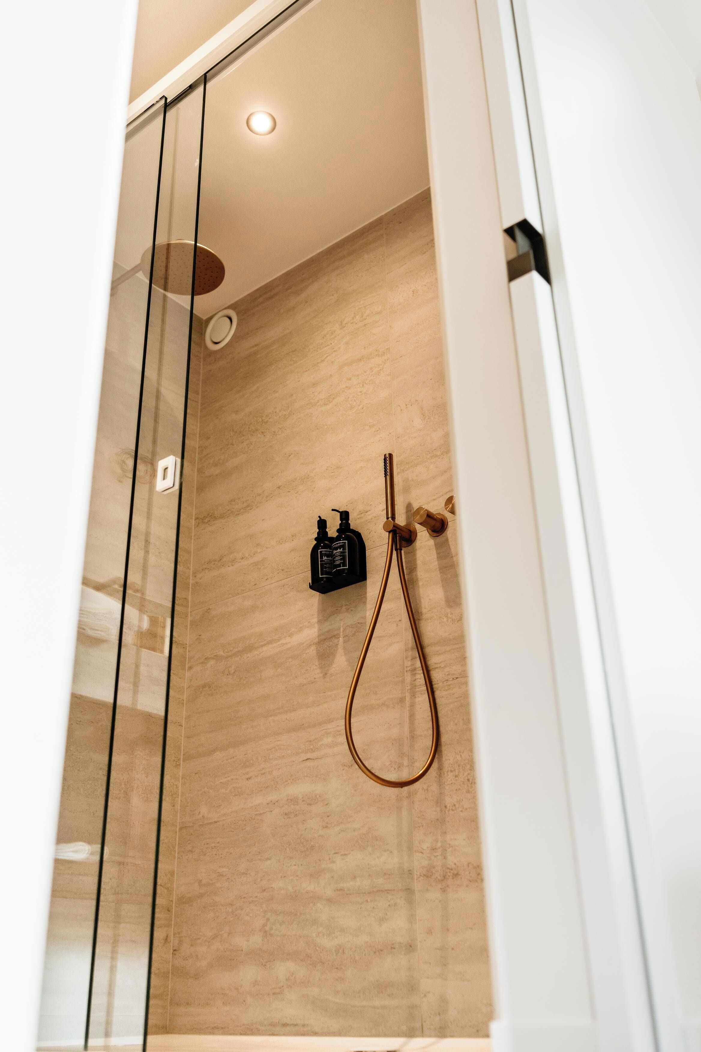 A modern shower with glass doors, a wooden wall, and a handheld showerhead.