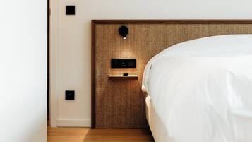 Un dormitorio moderno con cabecera de madera, cama blanca y mesita de noche con iluminación integrada.