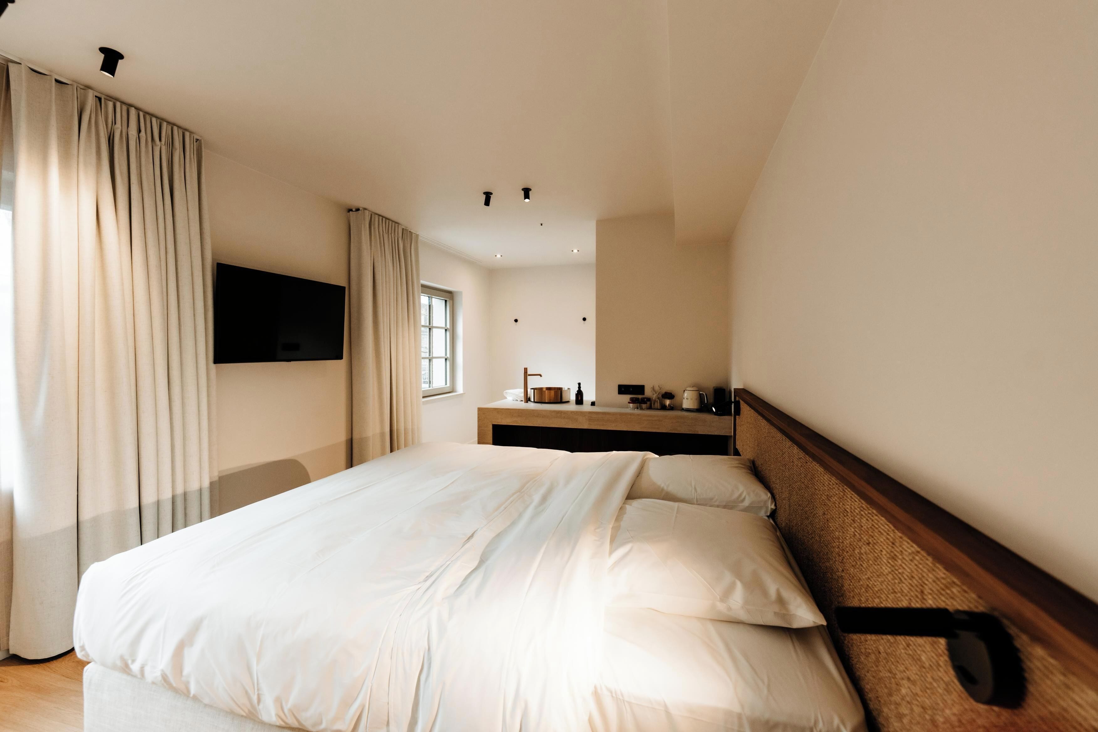 Quarto de hotel com cama grande, televisão de tela plana na parede, janela com cortinas e cabeceira de madeira.