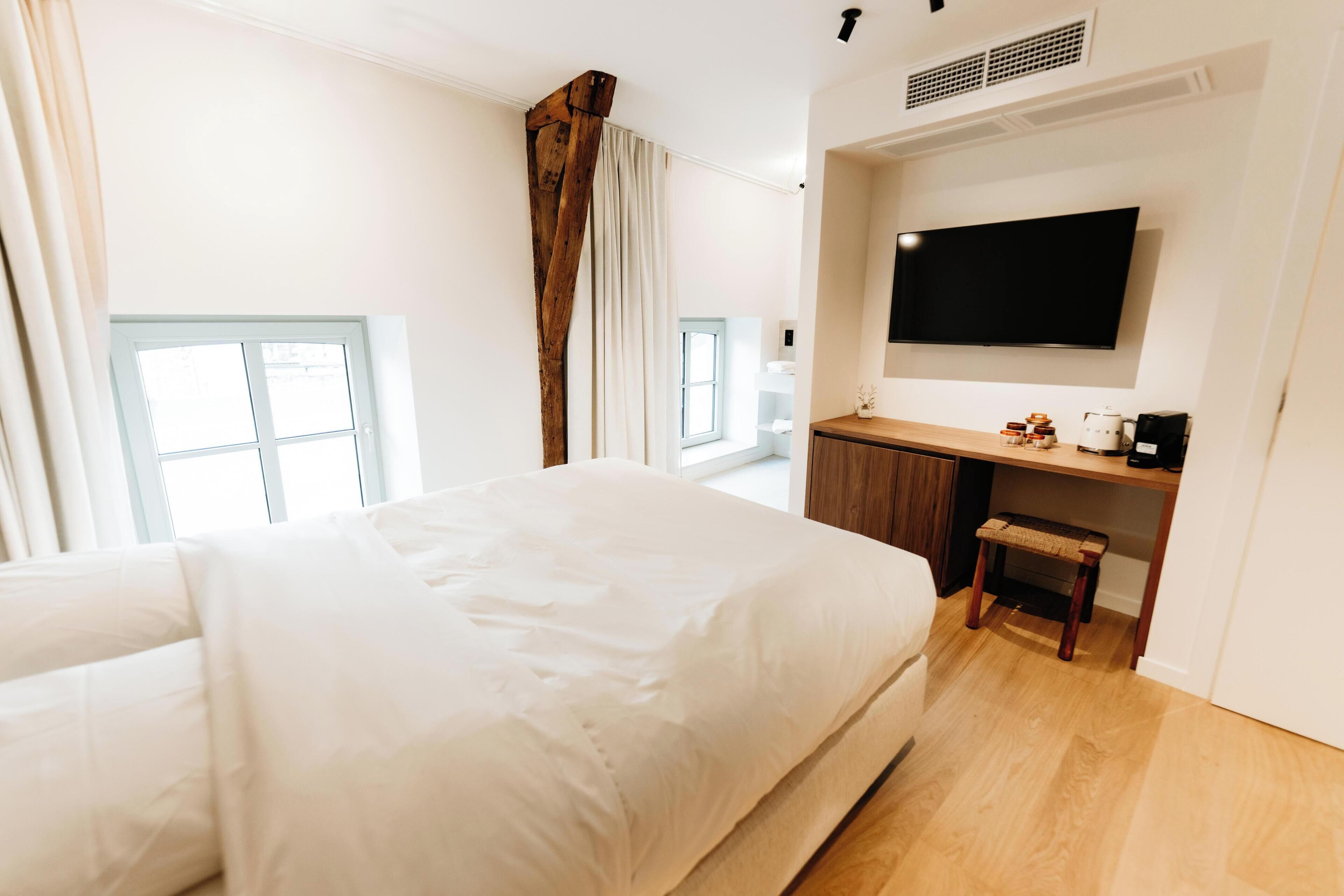 Une chambre d’hôtel moderne dotée d’un grand lit, d’un bureau avec une chaise, d’un téléviseur à écran plat et d’une fenêtre avec des rideaux.