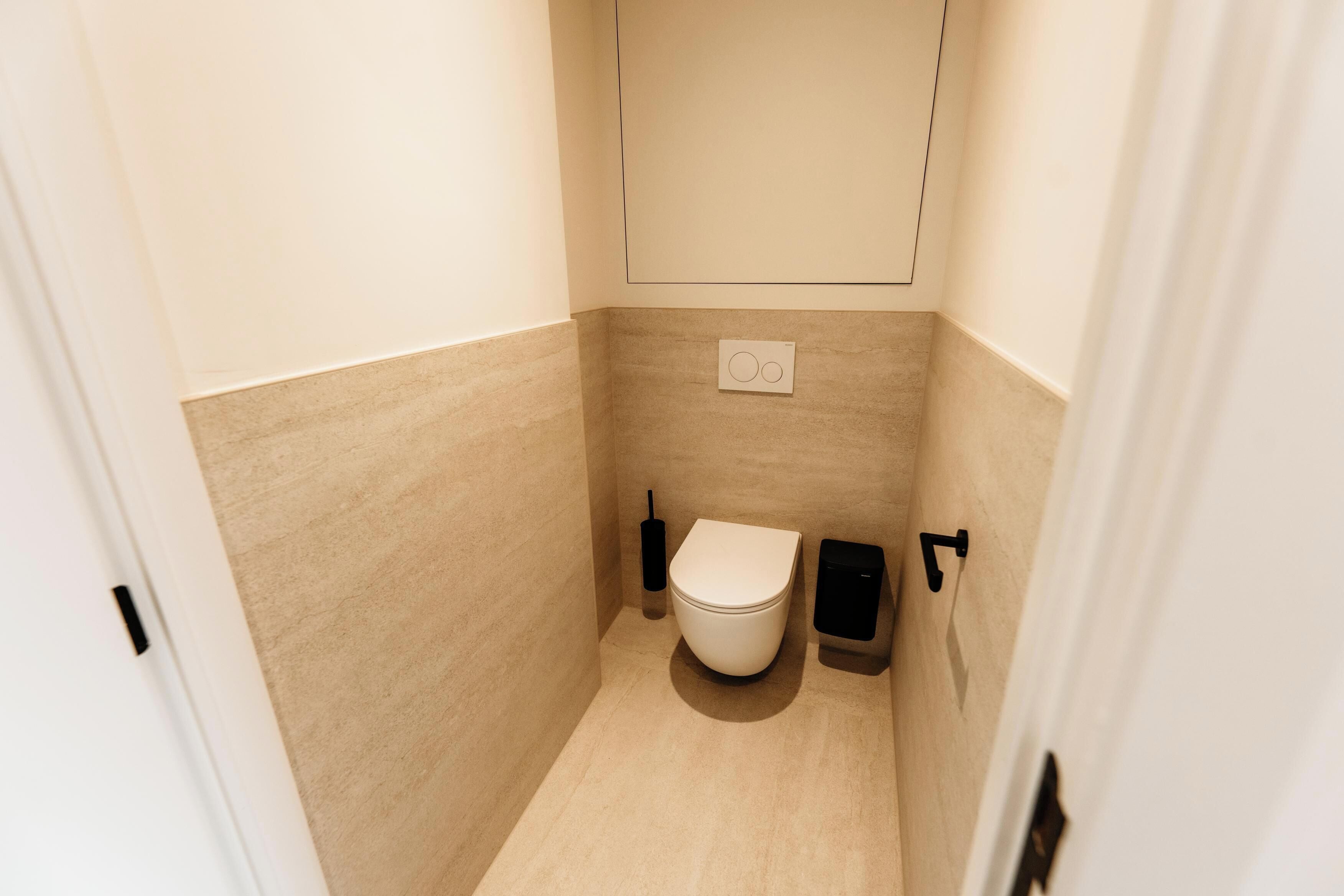 A small, modern bathroom with a toilet, bidet, and a wall-mounted light fixture.