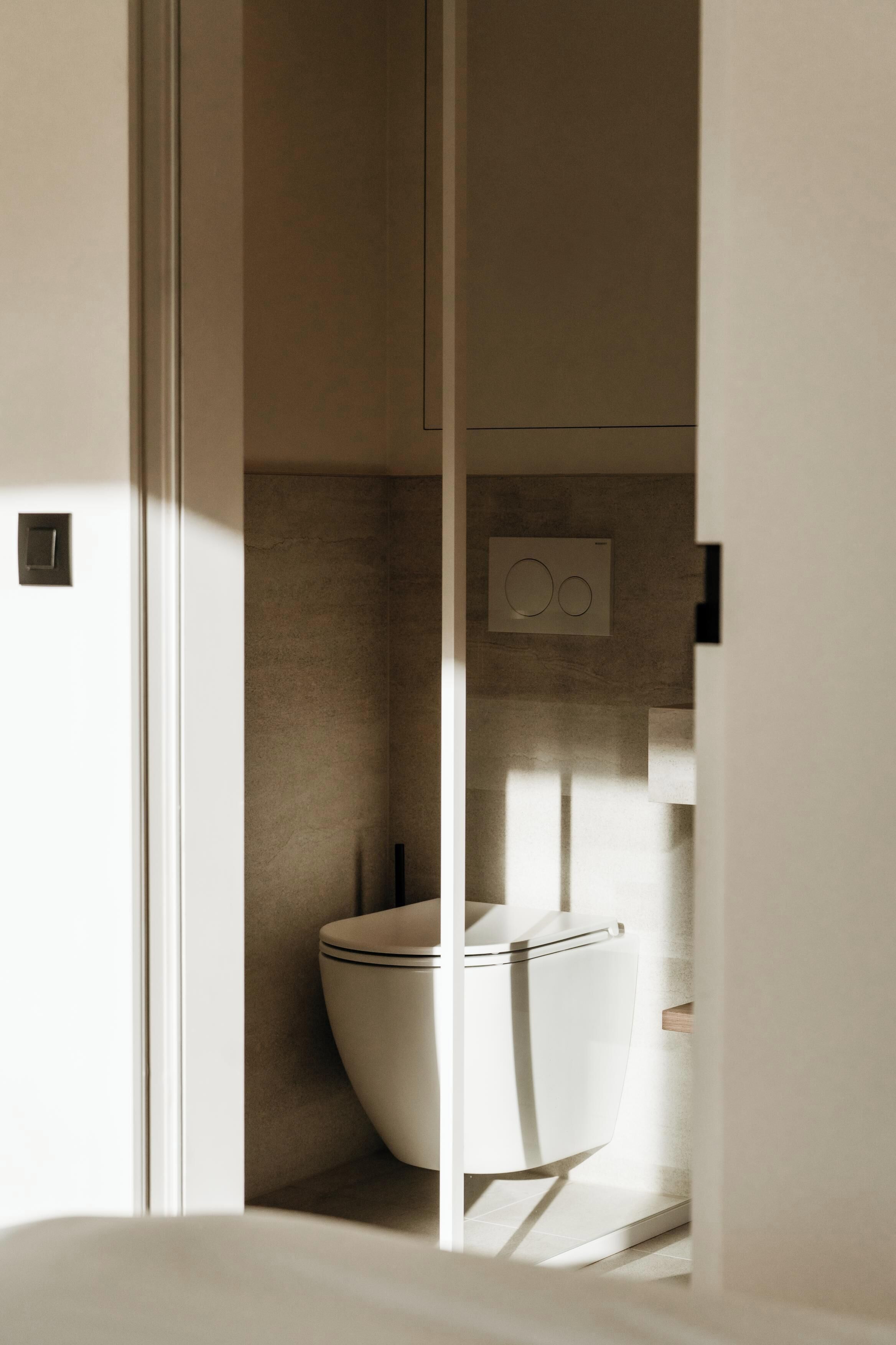 Un bagno moderno con un water, un pannello di controllo a parete e un corpo illuminante.