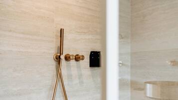 Een moderne badkamer met een douchecabine van glas, een goudkleurige douchekop en een zwarte kraan.