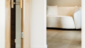 A room with a wooden floor, a white sofa, and a door leading to another room. - Alfred Hotel & Gastro Bar (Marche-en-Famenne)