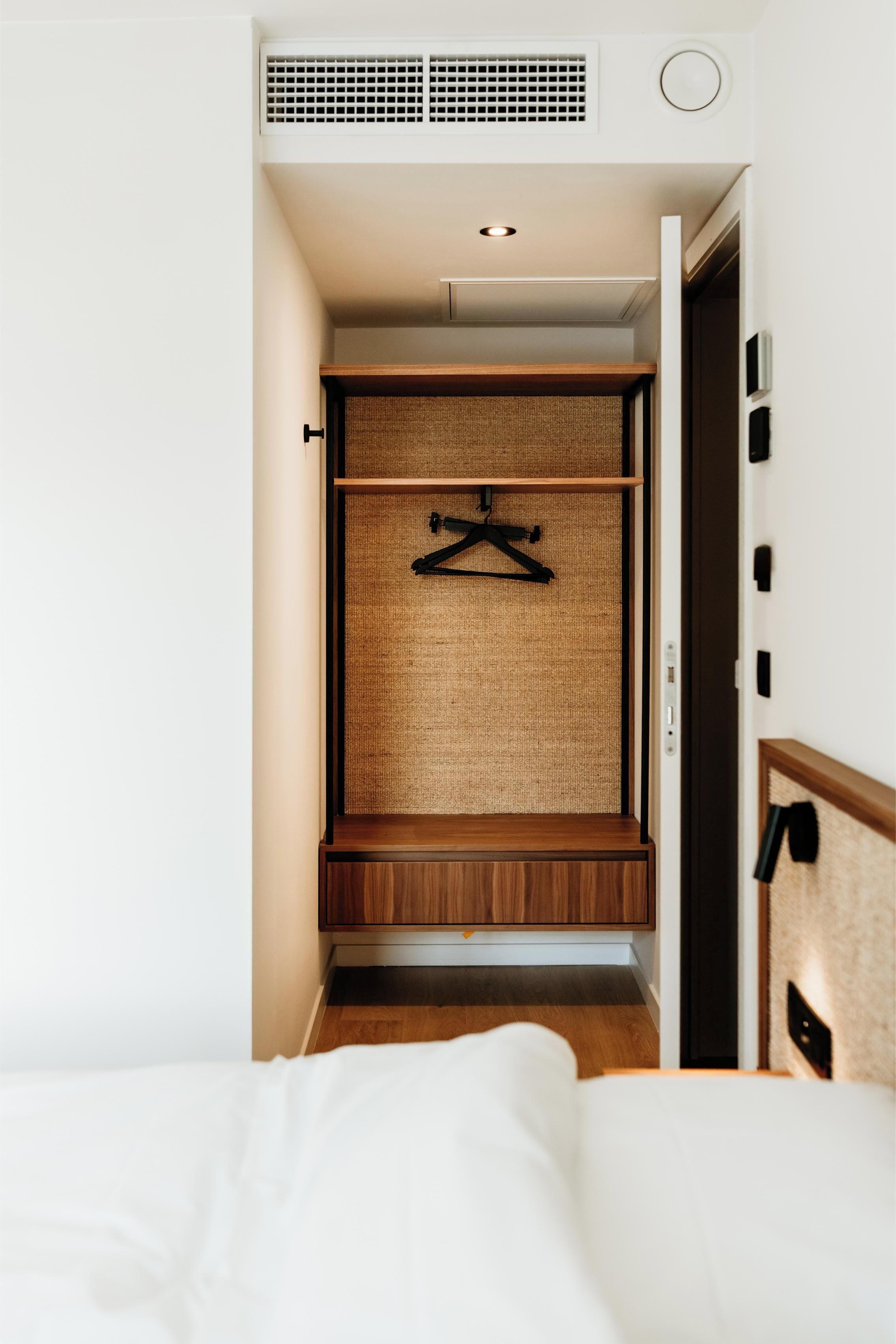 A bedroom with a bed, a wooden wardrobe with a hanging rack, and a small bench.