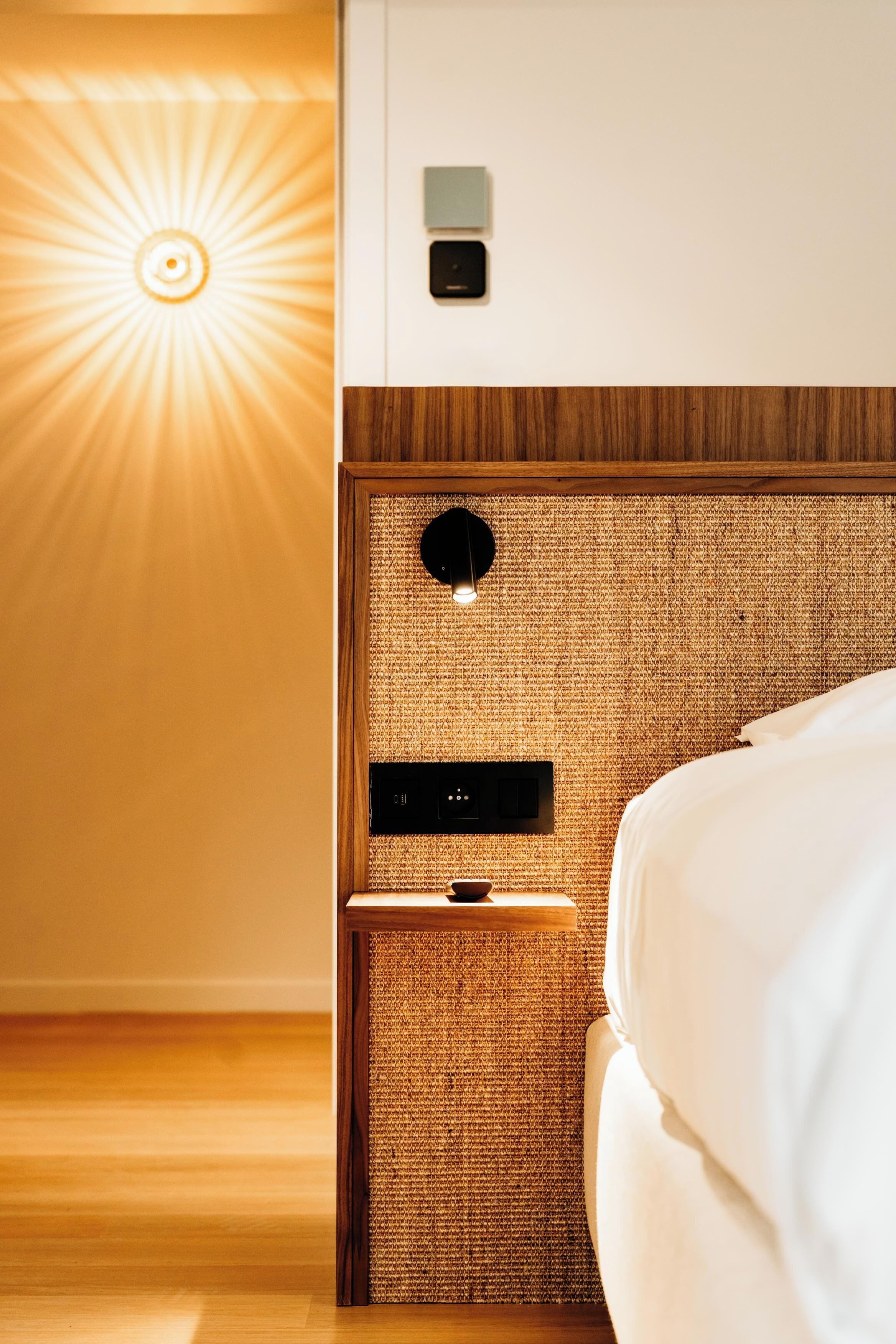 Een moderne hotelkamer met een houten hoofdbord, een ingebouwd bedieningspaneel en een wandlamp.
