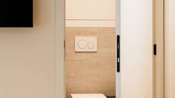Een hotelkamer met een bed, een aan de muur bevestigde televisie, een toilet en een deur naar een andere kamer.