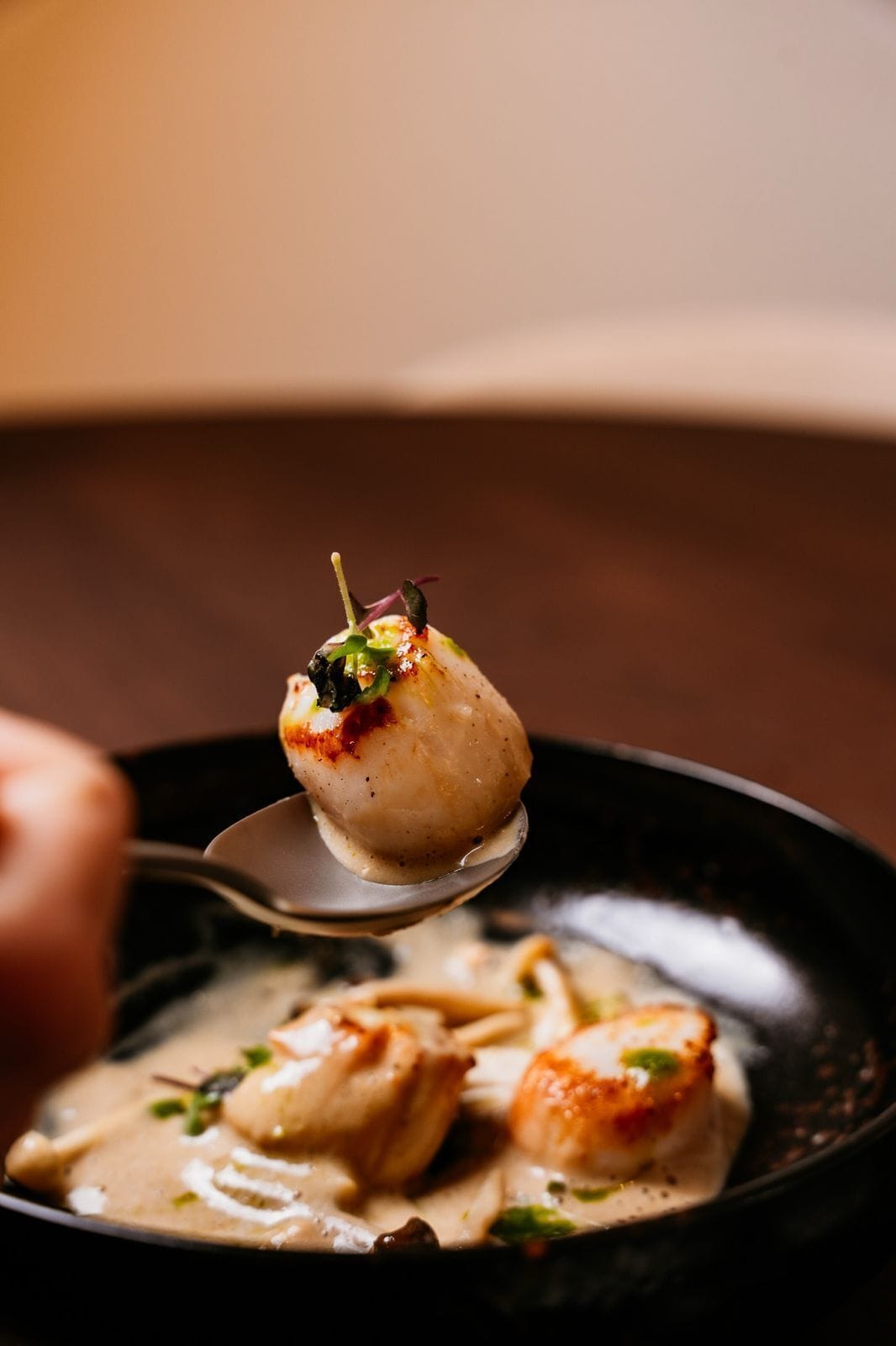 A spoonful of scallops with a garnish on a black plate.