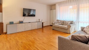 Een moderne woonkamer met een flatscreen televisie aan de muur, een zithoek en een houten vloer.